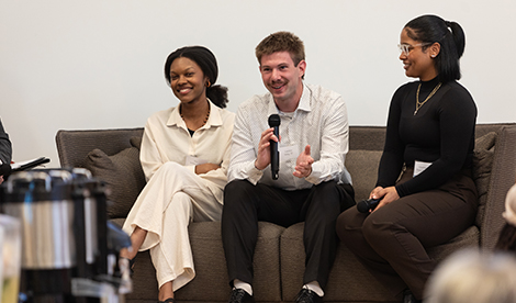 3 students sit and smile. One holds a microphone.