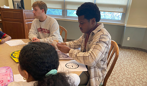 Roberts and elementary students sit around a table together