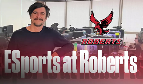 A man smiles among computers. The Roberts athletics logo and the words Esports at Roberts