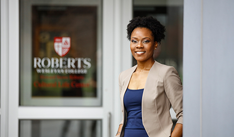 A woman smiles in front of a door that has the Roberts logo