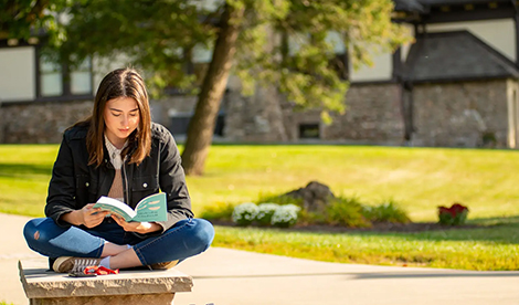A young woman reads a book outside on campus