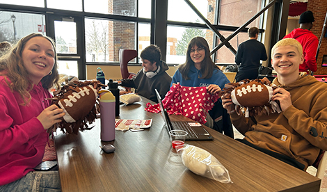 Students sit around a table and smile with pillows