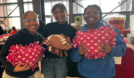 3 students hold pillows and smile