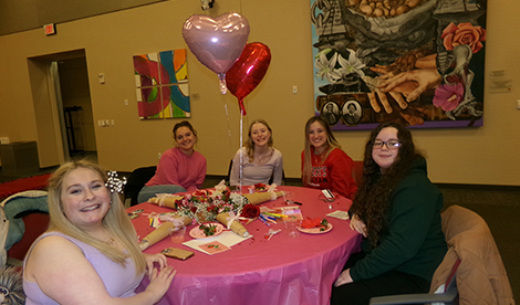 Students sit around a table with baloons and desserts