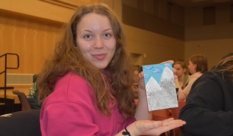 A young woman holds a painting while smiling