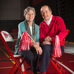 A man and woman smile with red pompoms